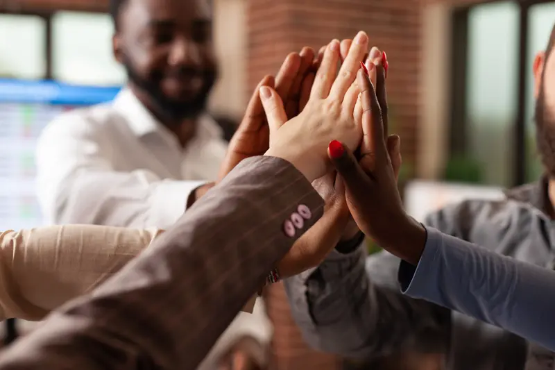 A group of business individuals exchanging high fives, symbolizing unity and teamwork in a professional setting.